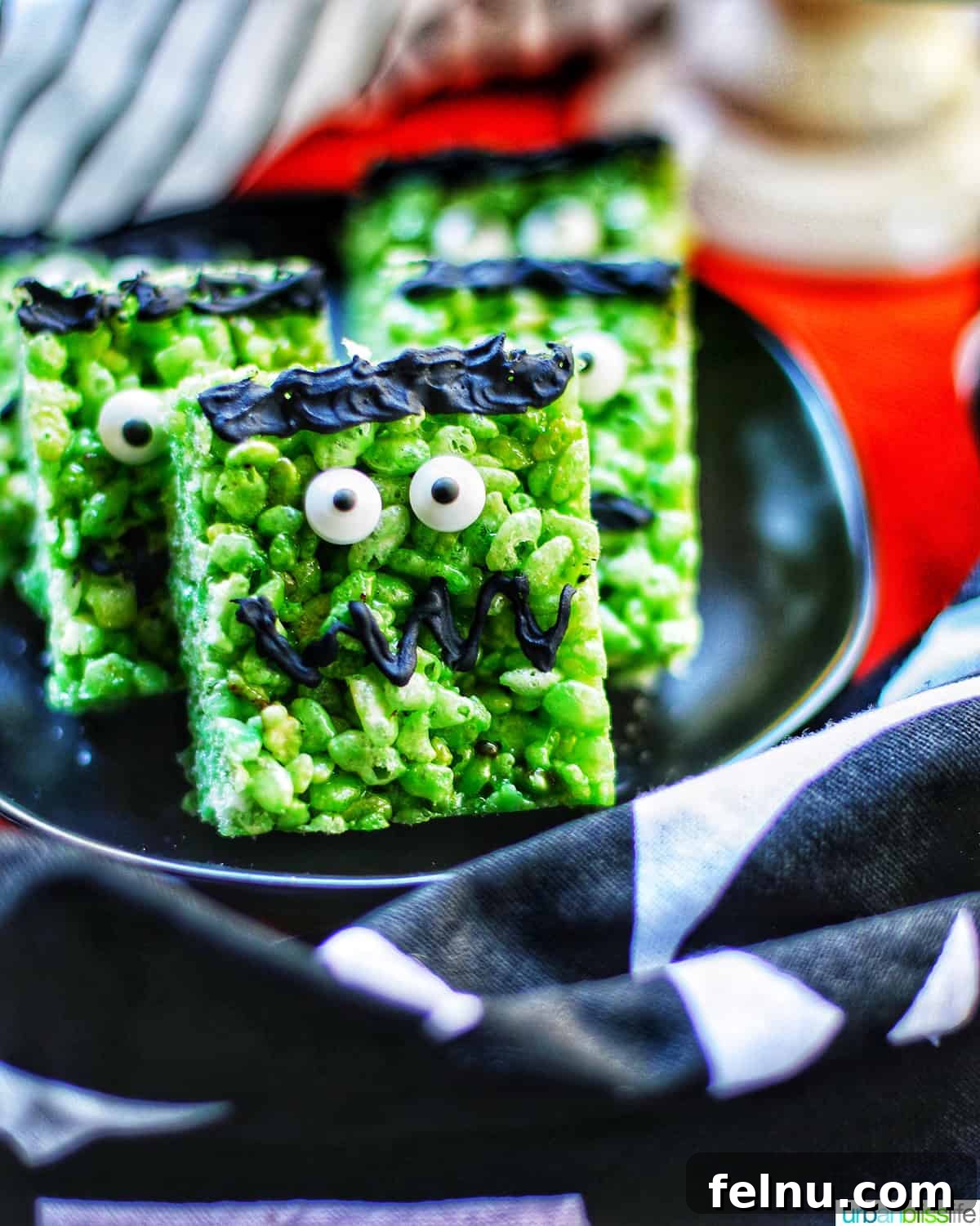 Frankenstein's Monster Munch 2 Close up of Frankenstein Rice Krispie Treats on top of black plates and orange background, showcasing their fun and spooky details.