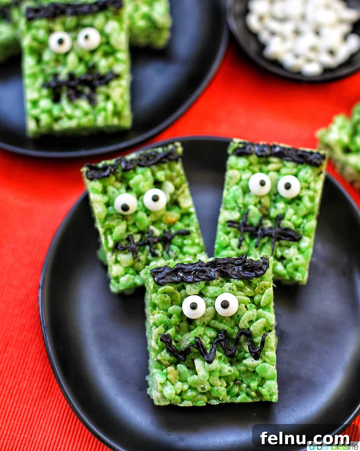 Frankenstein's Monster Munch 15 A group of Frankenstein Rice Krispie Treats elegantly presented on black plates against an orange background, perfect for a Halloween party.