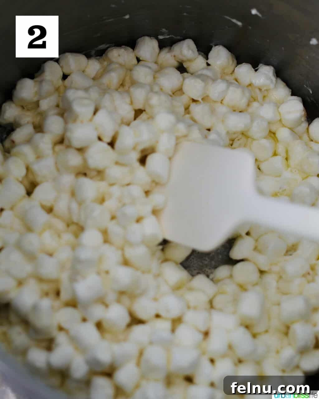 Frankenstein's Monster Munch 6 Mini marshmallows being added to melted butter in a large pot, beginning to combine.