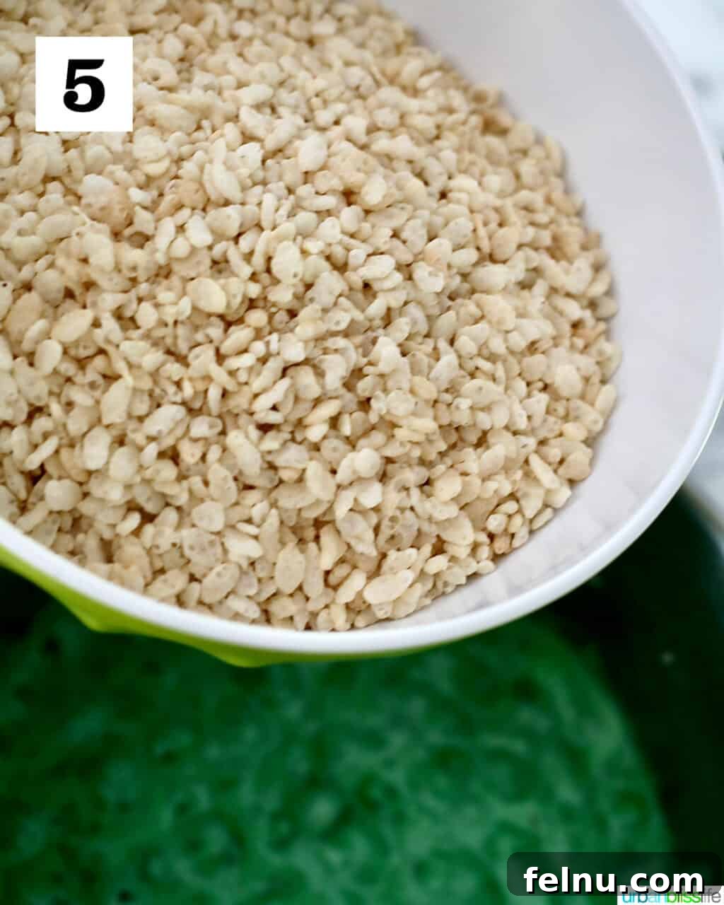 Frankenstein's Monster Munch 9 Pouring Rice Krispies cereal into the vibrant green marshmallow mixture in a large pot.