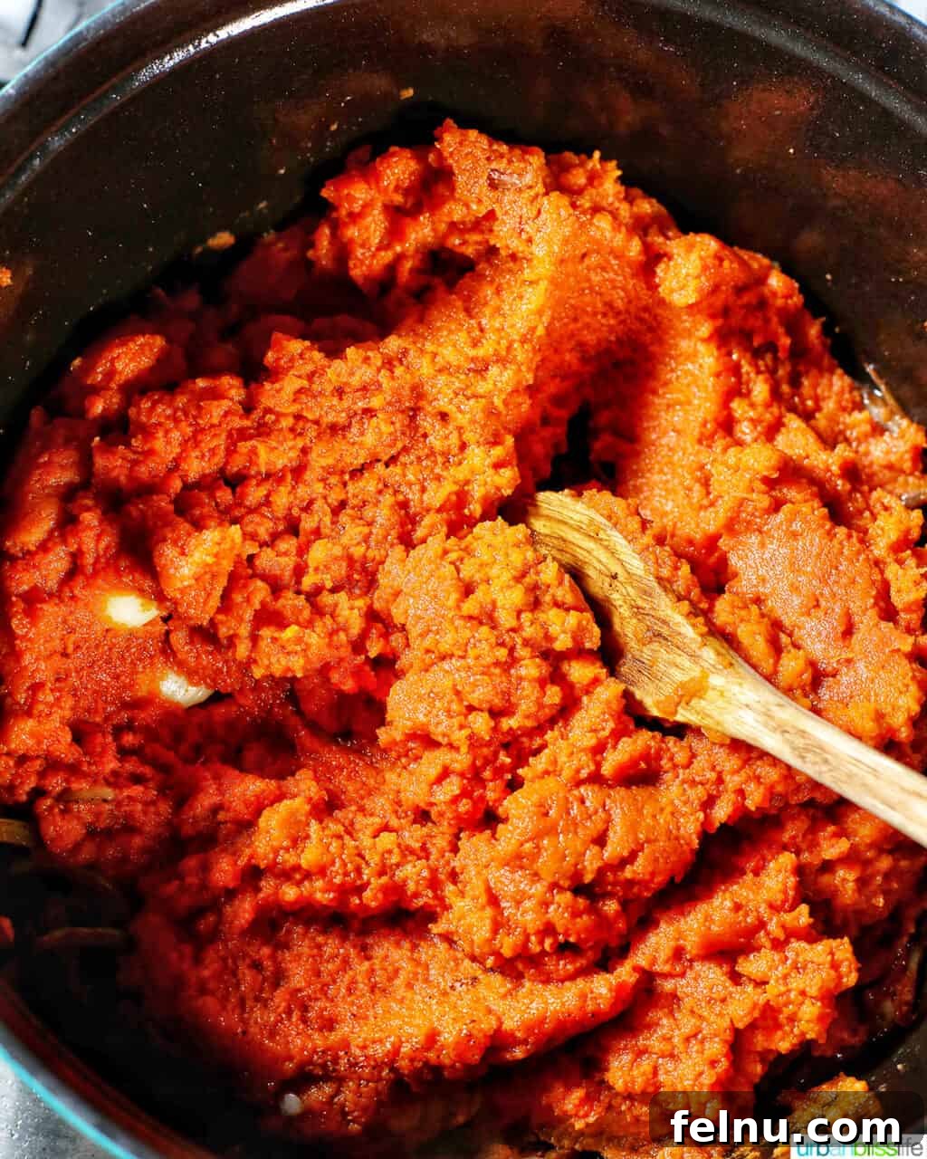 Pumpkin puree being added to the pot with sautéed onions, garlic, and spices, ready to be mixed into the soup base.