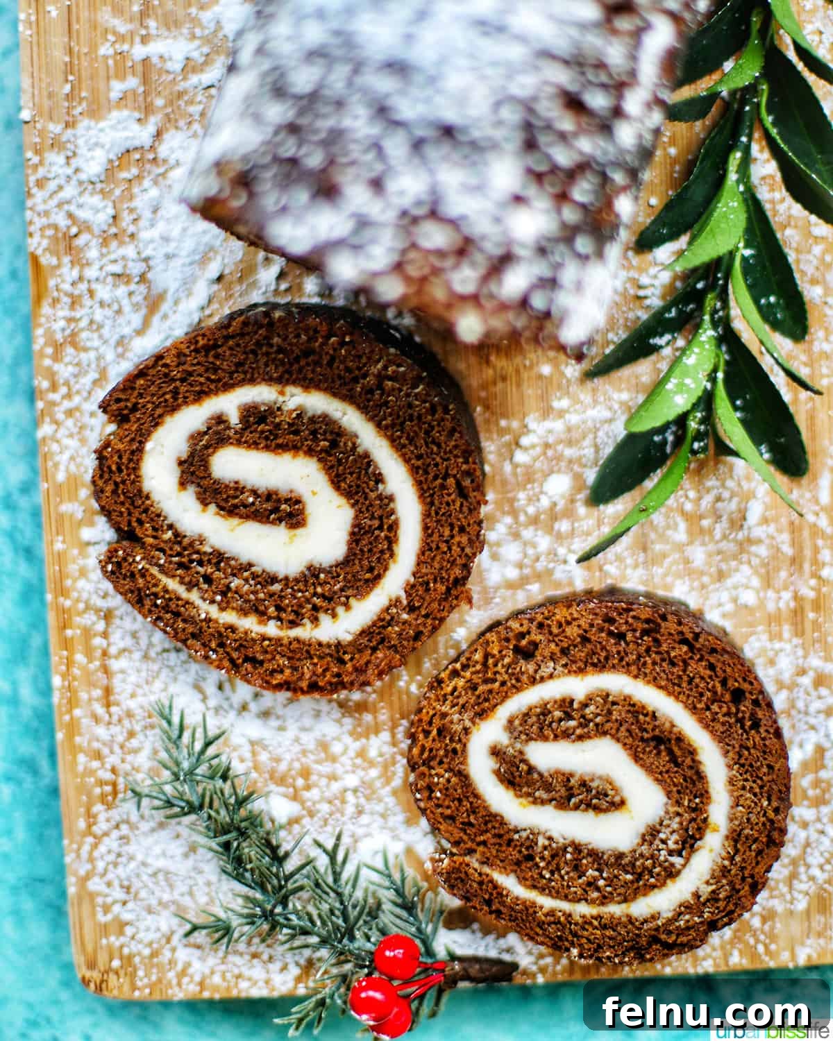 Gingerbread Swirl Cake 3 Close-up of two slices of Gingerbread cake roll with holiday trimmings and cream cheese filling, next to Christmas decorations.