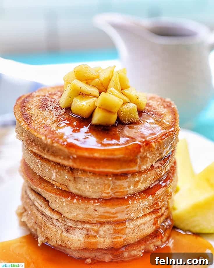 Fluffy Apple Cinnamon Pancakes stacked high, drizzled with syrup.