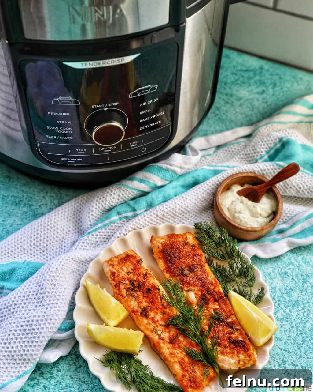 Perfect Air Fryer Salmon Every Time 4 Air fryer salmon served on a plate with dill and lemon wedges, with a Ninja Foodi air fryer in the background.