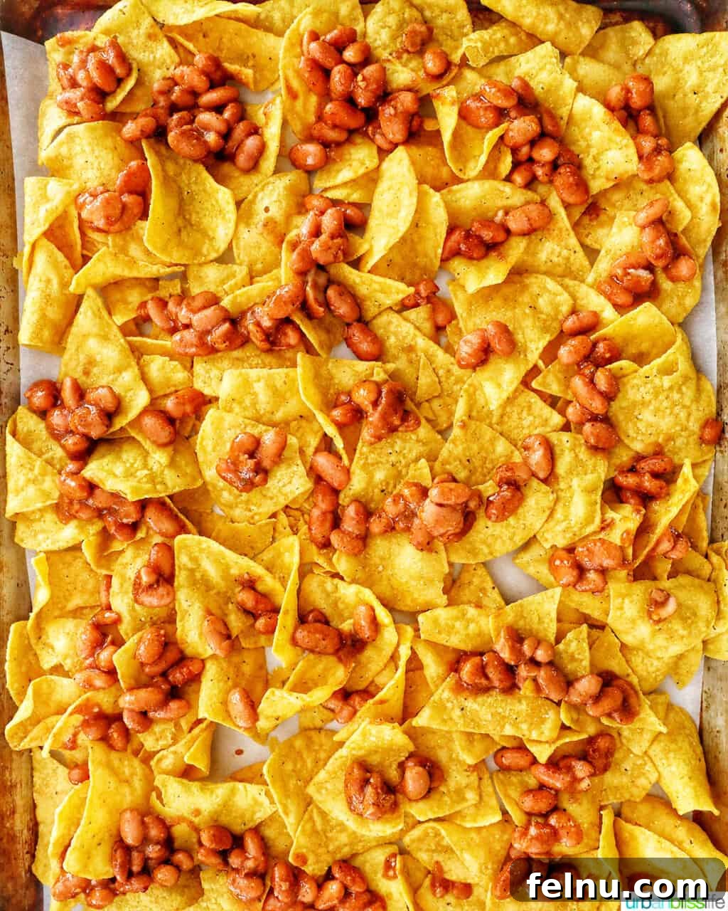 One-Pan Veggie Tex-Mex Nacho Fiesta 7 Tortilla chips partially covered with seasoned pinto beans, preparing for baking