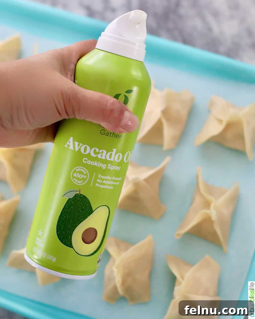 Perfectly Crispy Air Fryer Crab Rangoon 16 Avocado oil spray being used on air fryer crab rangoons