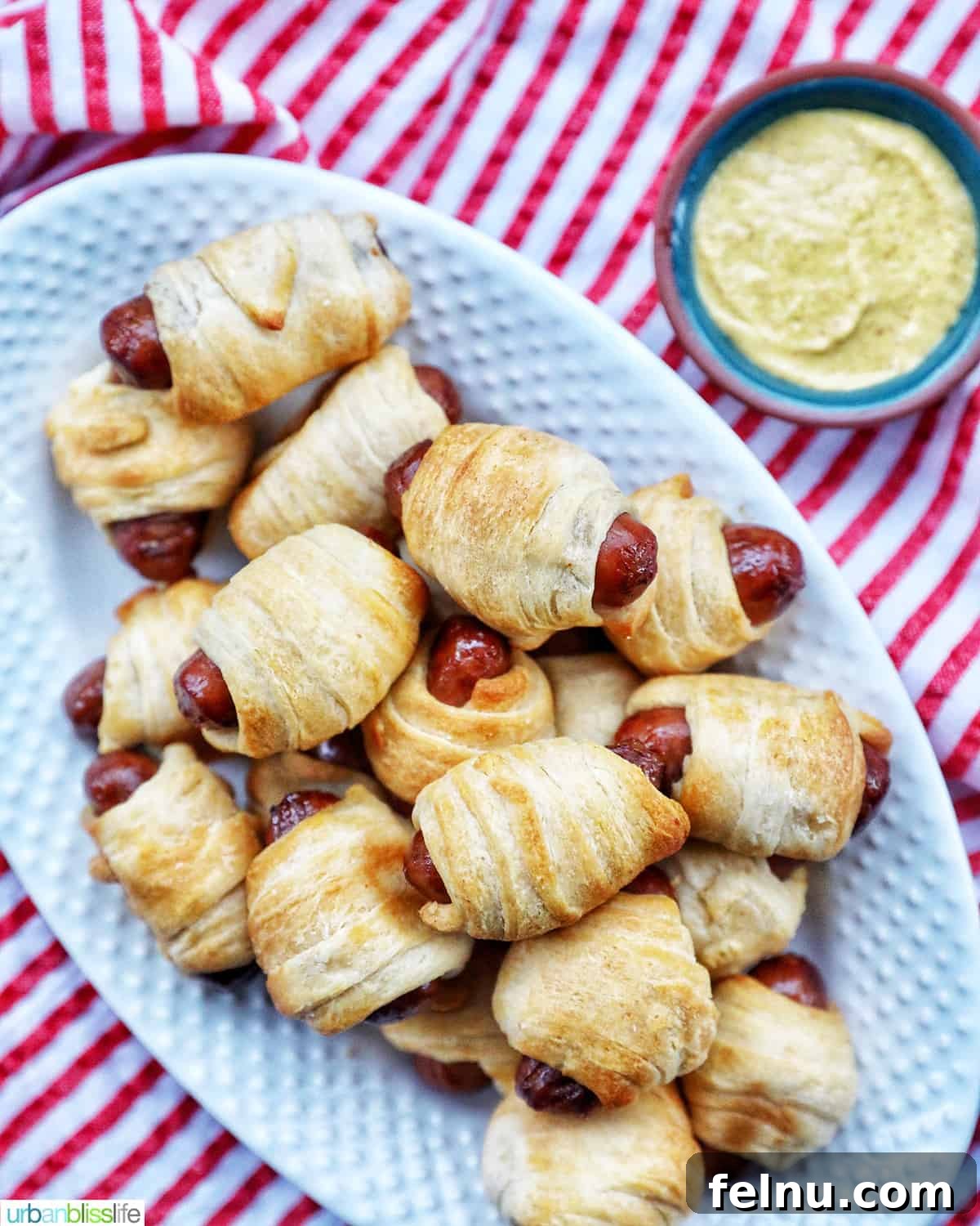 Crispy Air-Fried Pigs in a Blanket 3 dozens of Air Fryer Pigs in a Blanket on a plate with side of mustard on a red and white napkin.