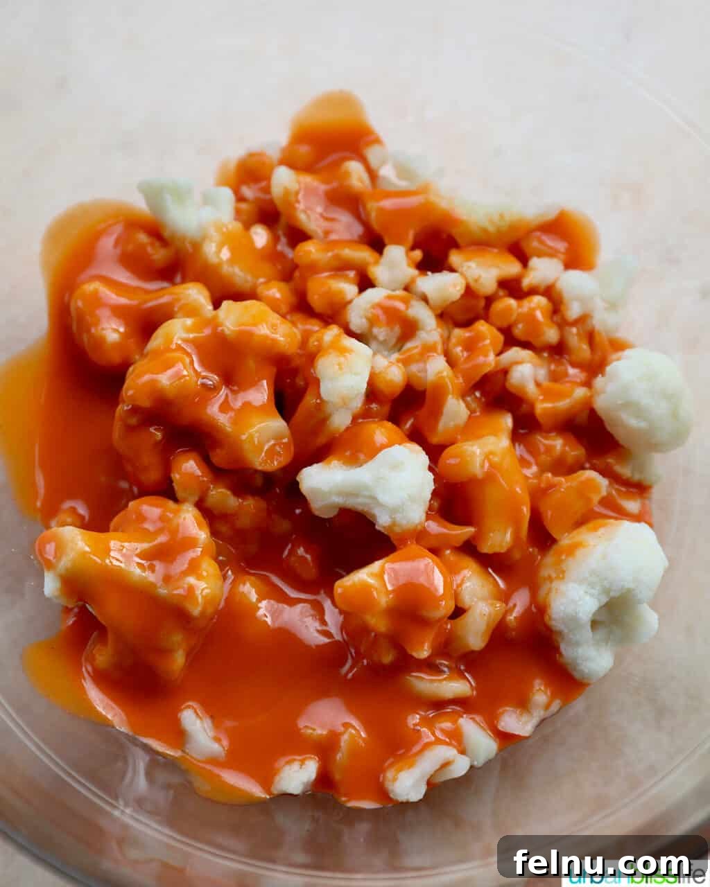 Fiery Air-Fried Cauliflower Poppers 7 Buffalo sauce being added to cauliflower florets in a bowl.