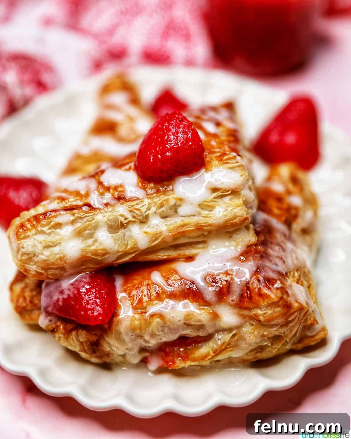 Flaky Strawberry Pockets 2 iced strawberry turnovers stacked on a plate with fresh strawberries