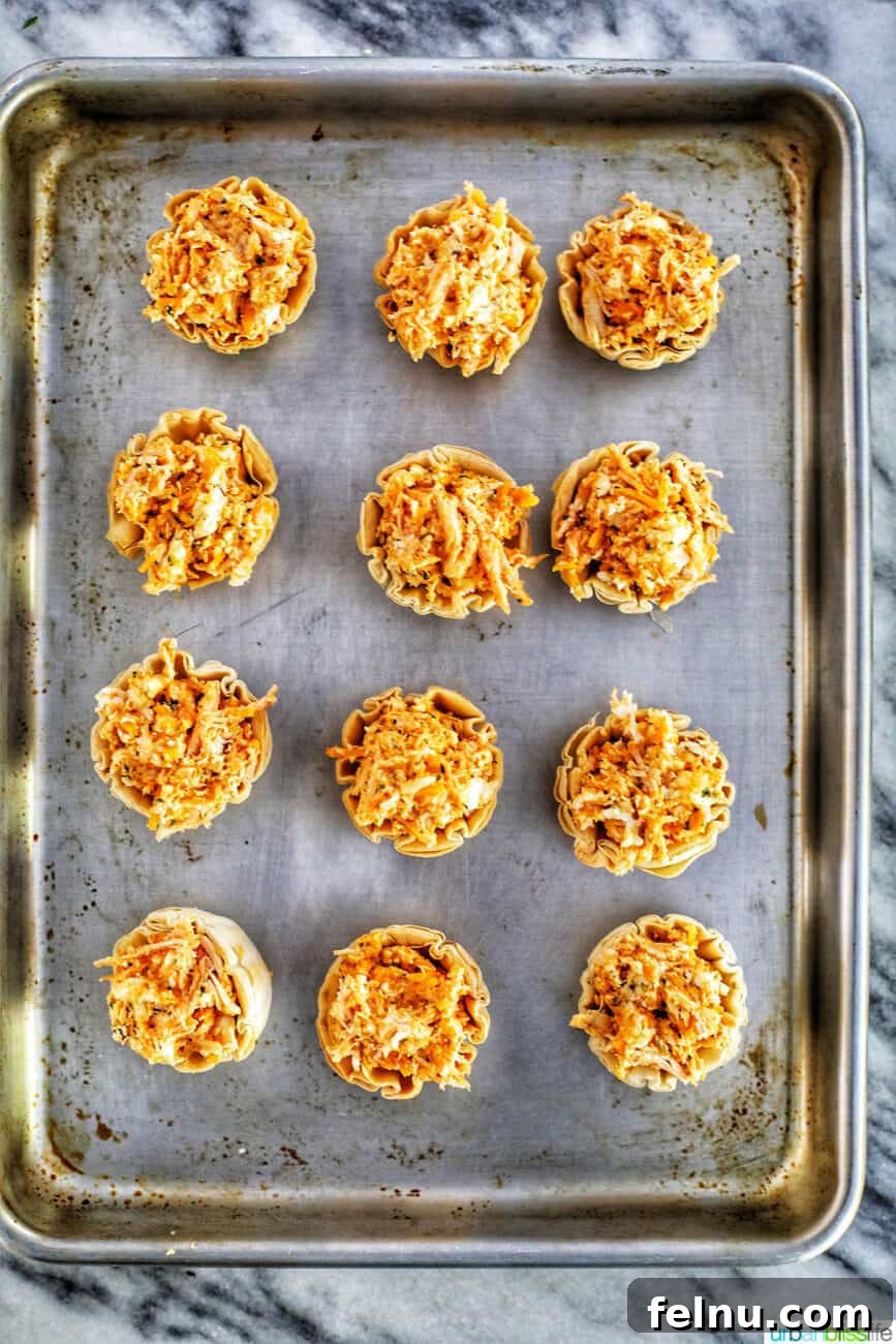 Kickin' Chicken Poppers 13 Buffalo Chicken Bites filled in phyllo cups on a baking sheet, ready for the oven.