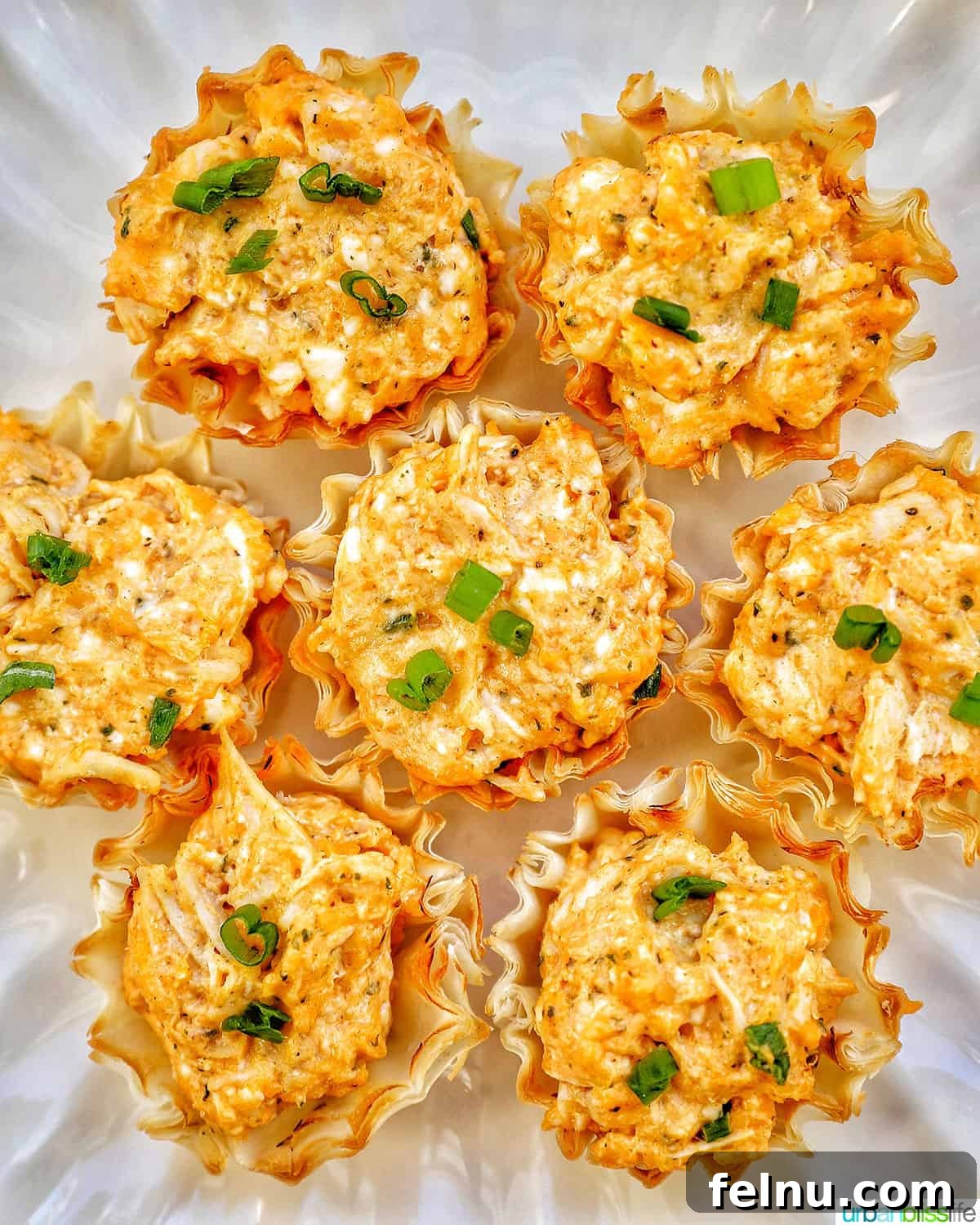 Spicy Buffalo Chicken Poppers 3 Close-up of several buffalo chicken bites adorned with finely chopped green onions on a white plate, highlighting their appetizing texture.