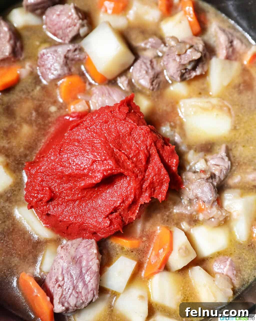 Adding tomato paste to beef caldereta.