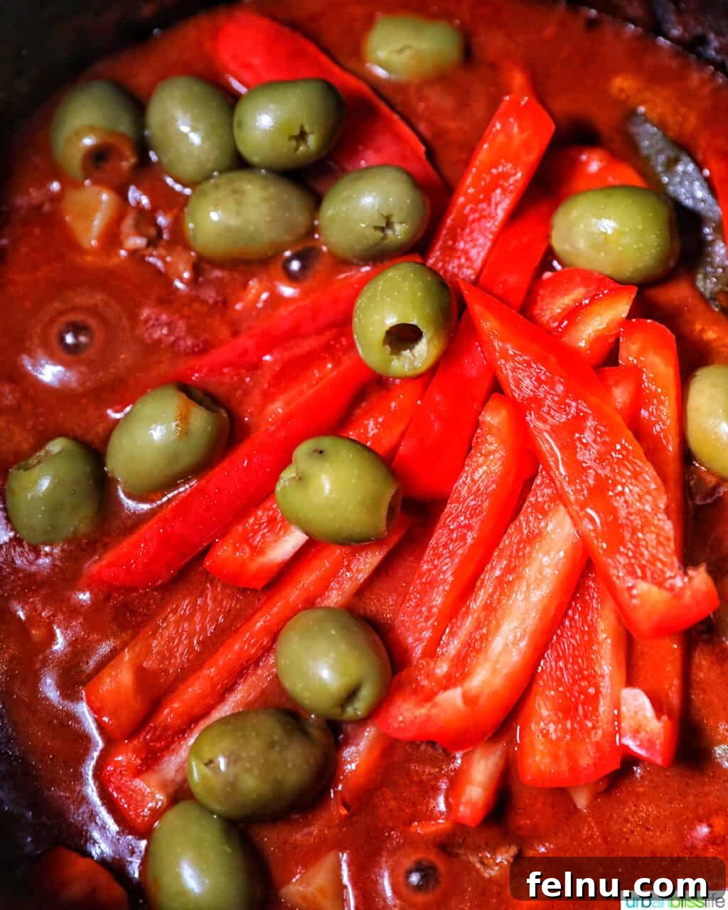 Adding red peppers and green olives to pot of beef caldereta.