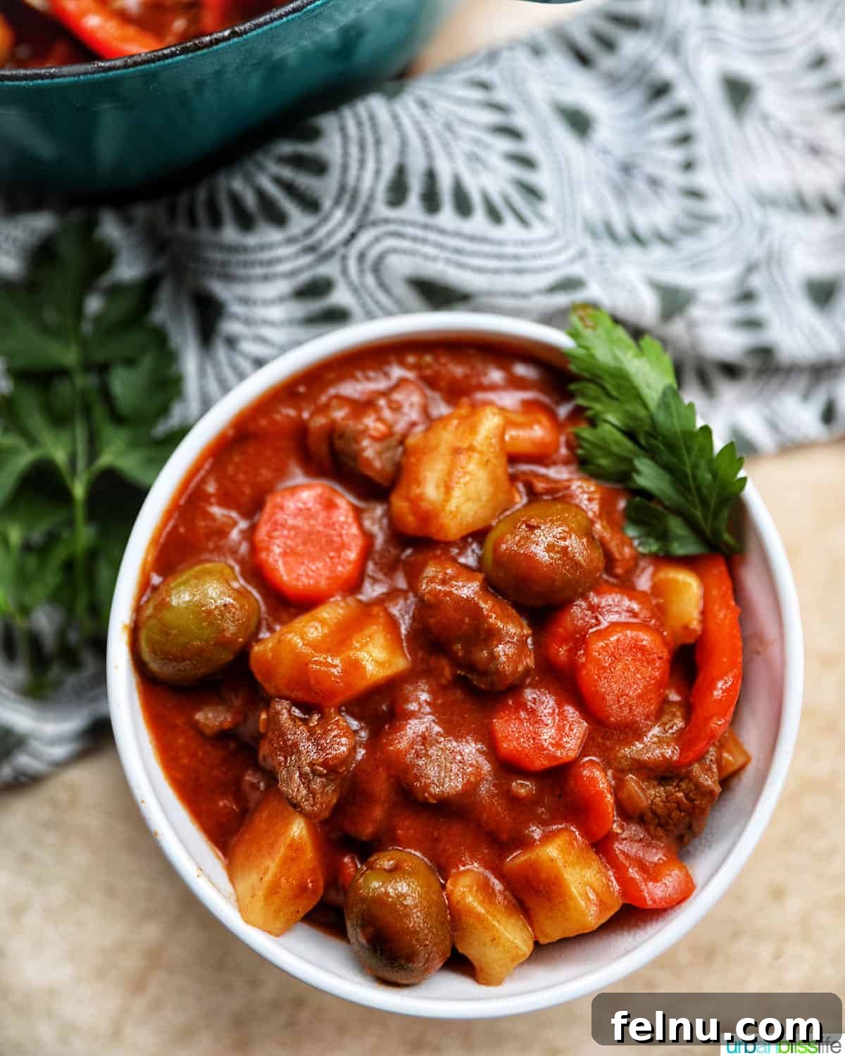 Single bowl of Filipino beef caldereta stew with potatoes, carrots, red peppers, and green olives.