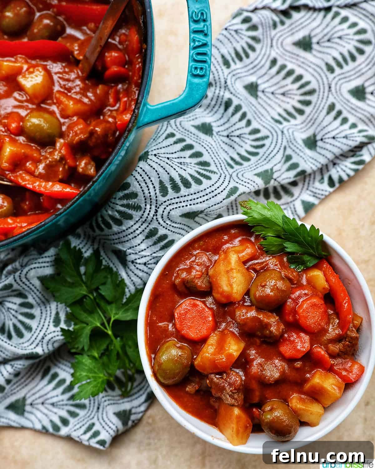 Beef caldereta in a bowl and a large blue Staub pot, featuring potatoes, green olives, red peppers, and tomatoes.