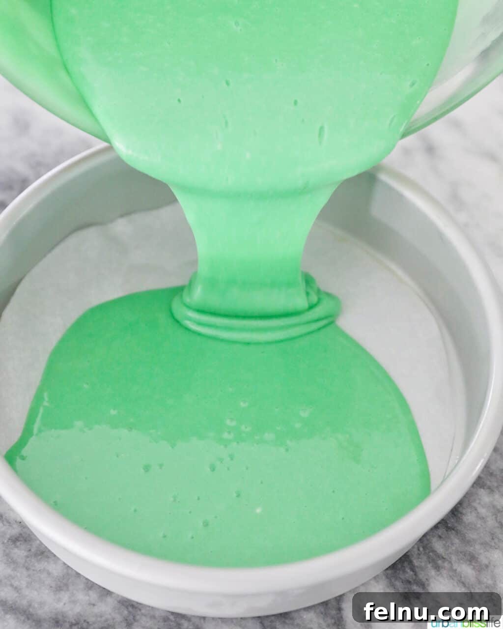 Emerald Velvet Delight with Tangy Cream Cheese 17 Green cake batter being poured into a prepared cake pan.