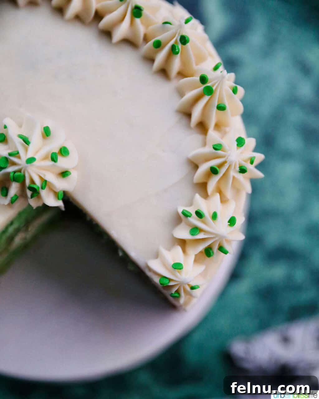 Emerald Velvet Delight with Tangy Cream Cheese 4 An overhead view of a beautifully frosted green velvet cake, adorned with edible decorations.
