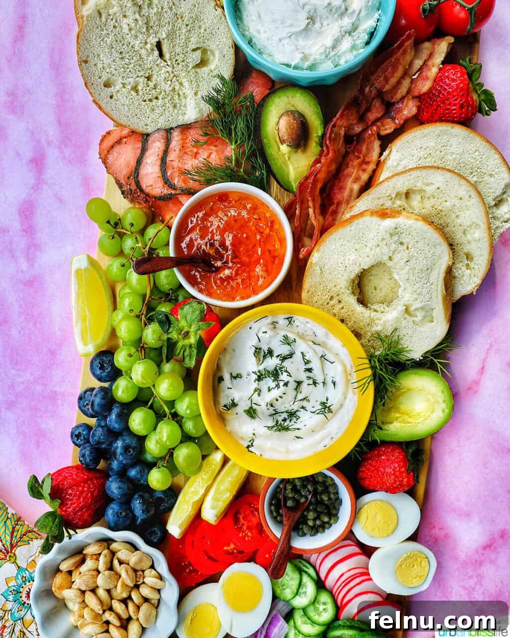 Brunch Grazing Platter 3 A bagel brunch board arranged on a pink backdrop, showcasing a colorful assortment of brunch staples.