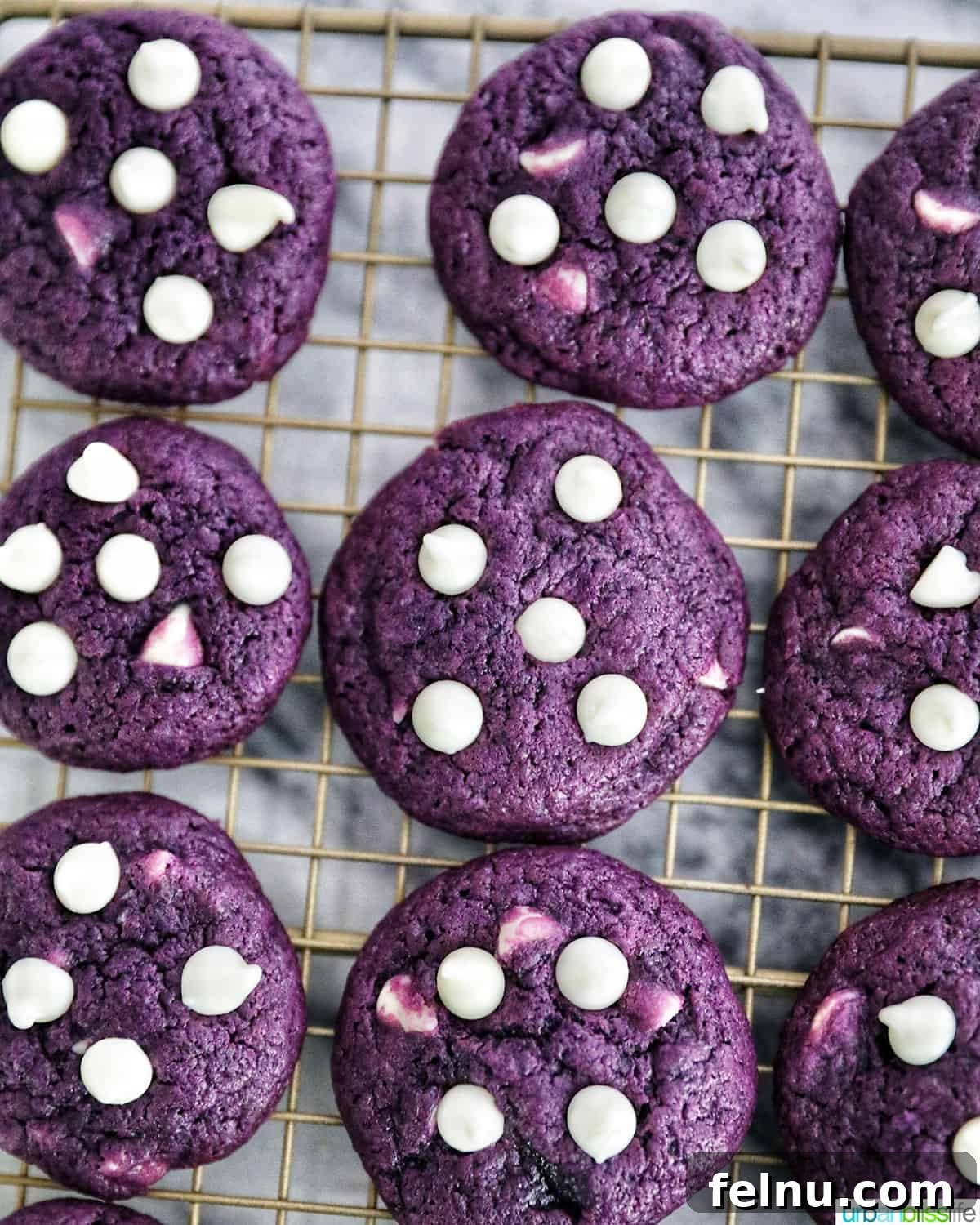 Ube and White Chocolate Dream Cookies 19 A batch of freshly baked Ube cookies cooling on a wire rack, placed on a marble tabletop.