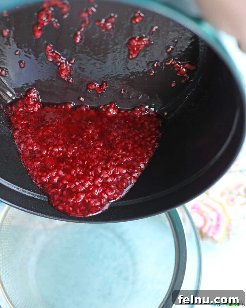 Raspberry Sparklers 11 Pouring the cooked raspberry mixture over a bowl lined with a fine mesh strainer.