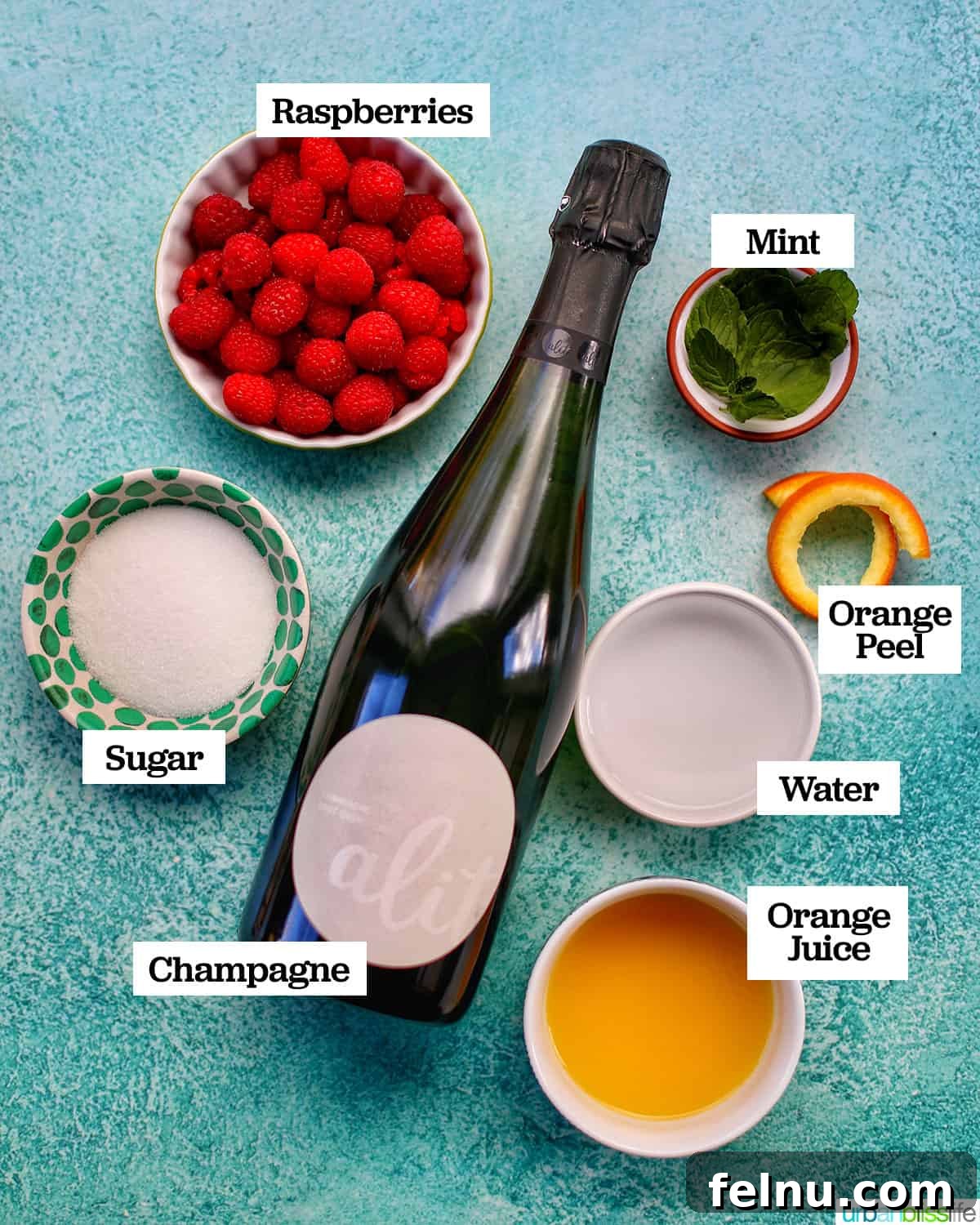 Raspberry Sparklers 4 The five main ingredients needed to prepare Raspberry Mimosas, arranged in bowls, with a glass of sparkling wine on a blue surface.