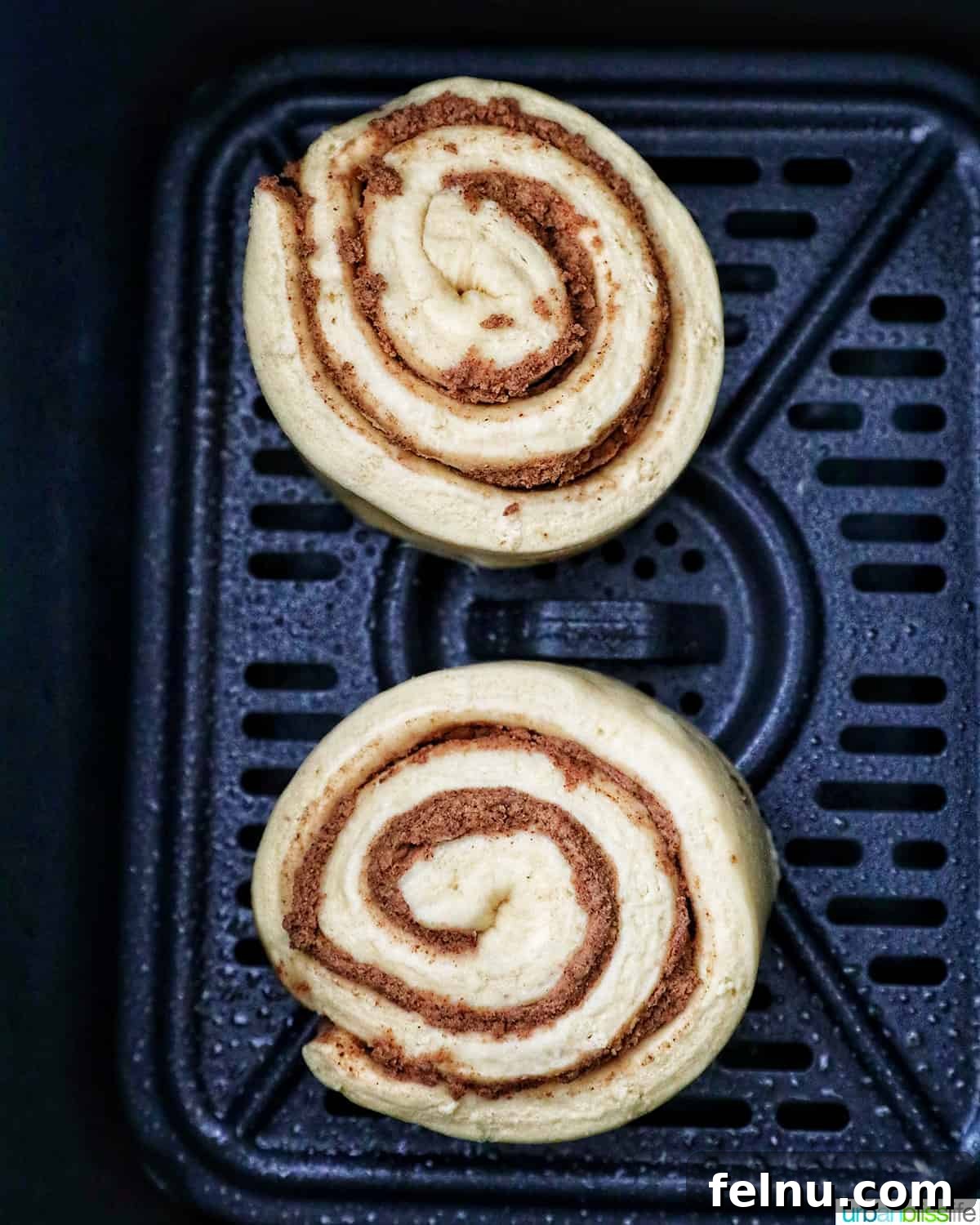 Golden Air Fryer Cinnamon Swirls 5 Two raw cinnamon rolls placed in an air fryer tray, ready for cooking