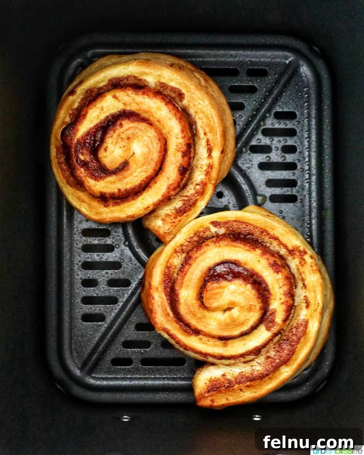 Golden Air Fryer Cinnamon Swirls 7 Two perfectly air fried cinnamon rolls in the air fryer basket, golden brown