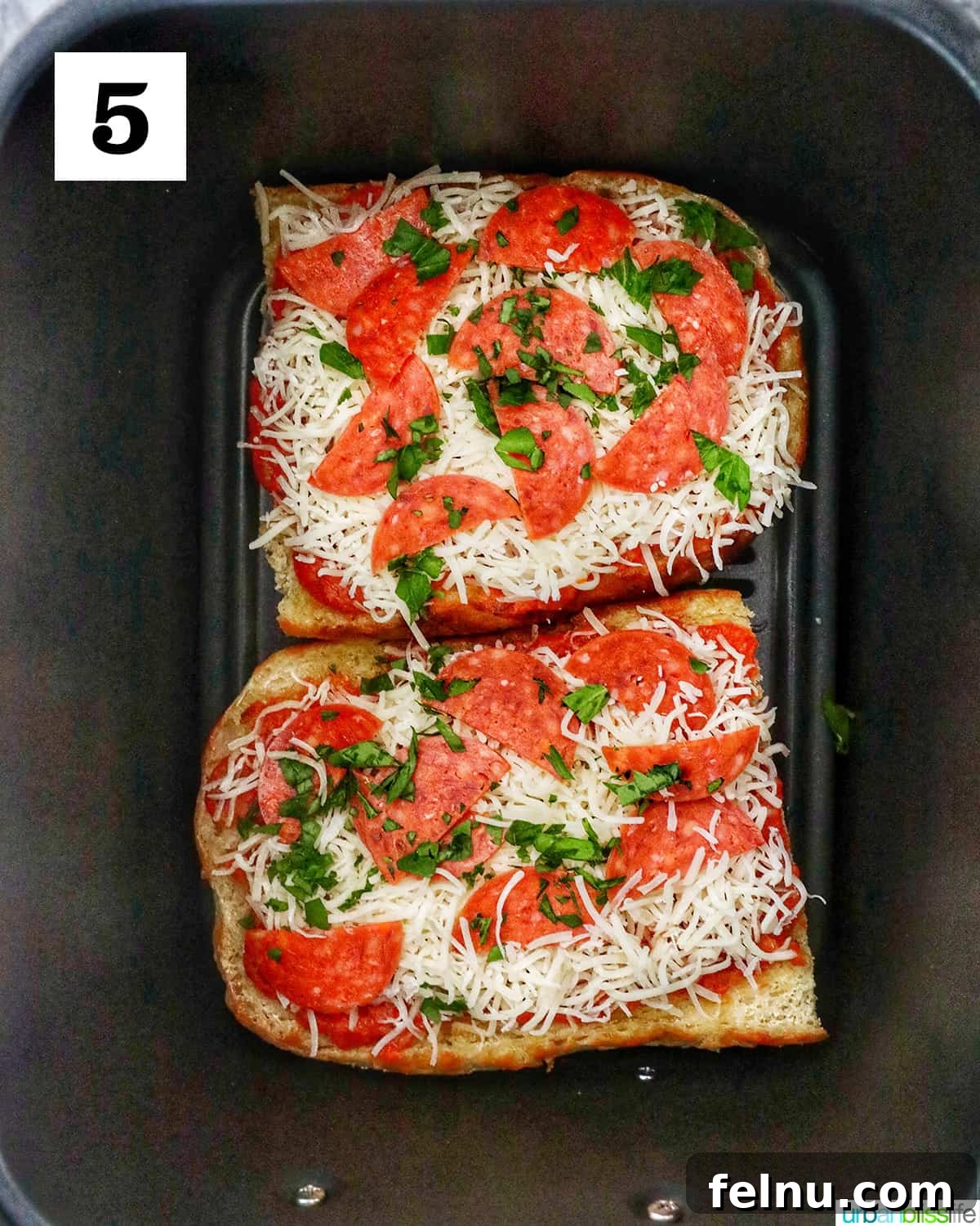 Crispy Air Fryer Pizza 11 Two French bread halves, fully loaded with pizza toppings, carefully placed back into an air fryer basket, ready for the final cook.