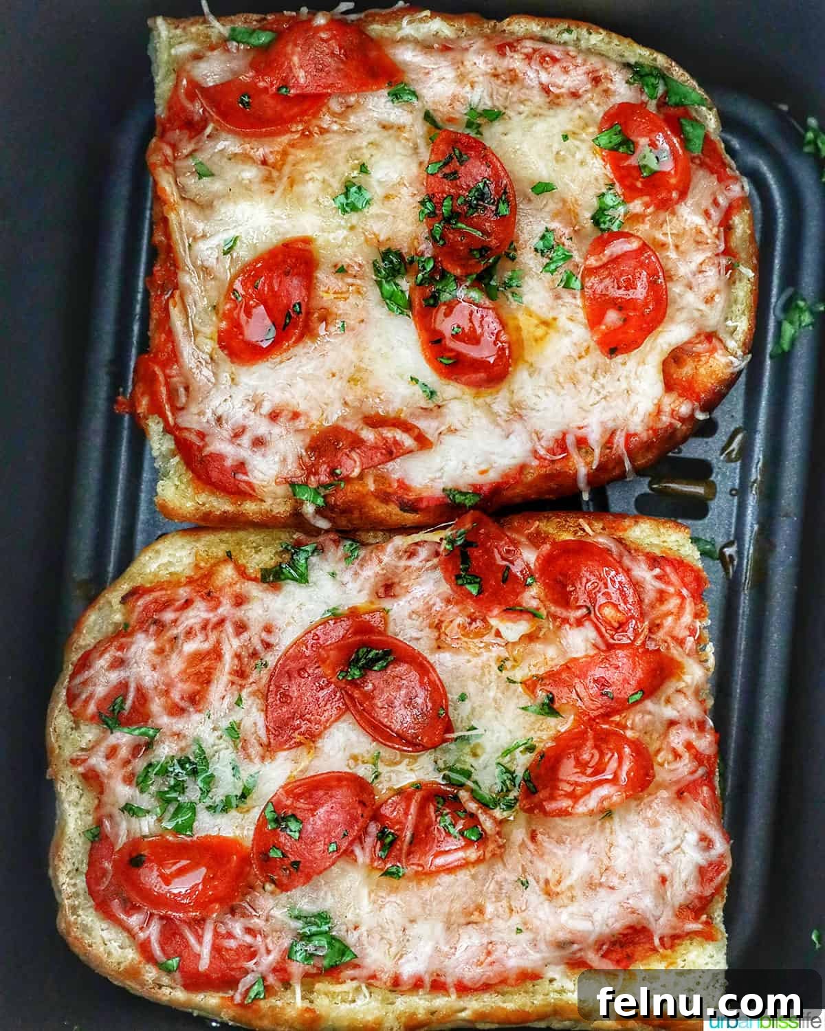 Crispy Air Fryer Pizza 13 Two half loaves of French bread pizza, beautifully golden with melted cheese, resting in an air fryer basket, indicating they are fully cooked and ready to enjoy.