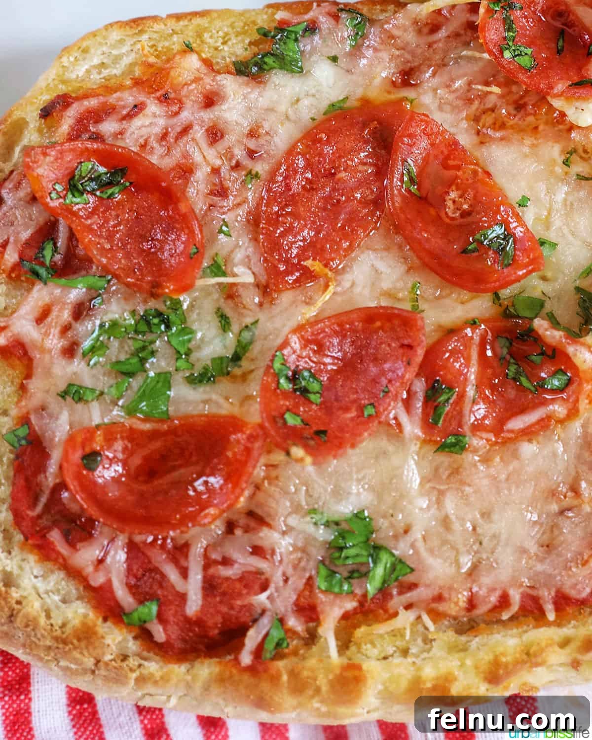 Crispy Air Fryer Pizza 3 A close-up shot of a single serving of pepperoni French bread pizza, garnished with fresh parsley and melted cheese, placed on a festive red and white striped napkin.