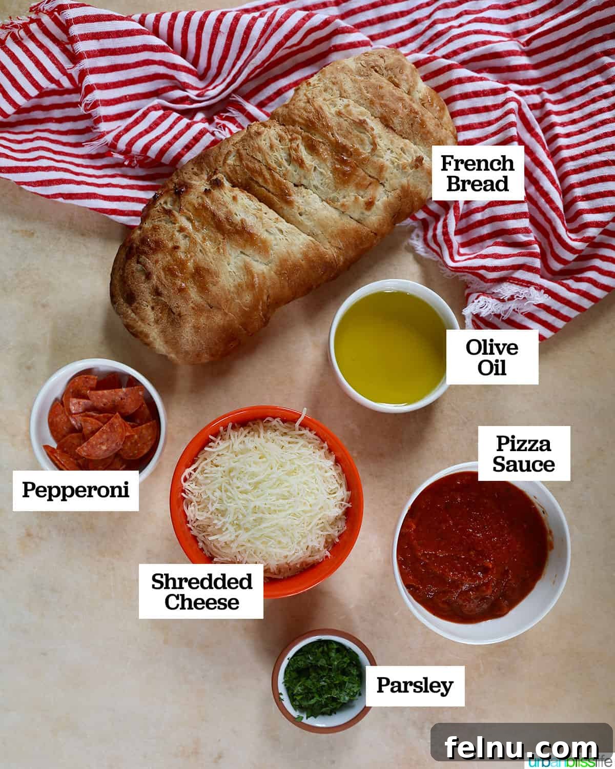 Crispy Air Fryer Pizza 4 A collection of ingredients for making air fryer French bread pizza, including a fresh loaf of French bread, bowls of pizza sauce, shredded cheese, and pepperoni, arranged on a marble countertop with a red and white napkin.