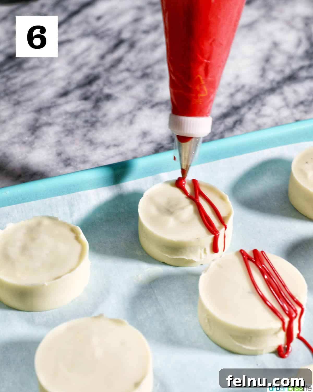 Fourth of July-Themed Oreo Delights 12 Red frosting being piped onto white chocolate covered Oreo cookies on parchment paper.