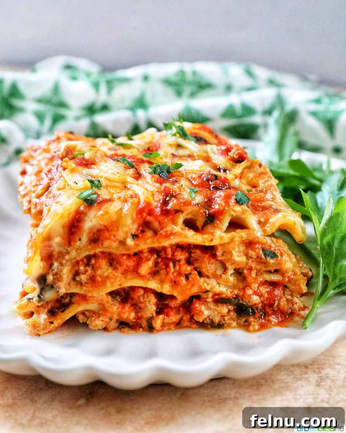 Creamy Vegan Lasagna 2 side view of multi-layered dairy free lasagna on a white plate with green and white napkin in background.