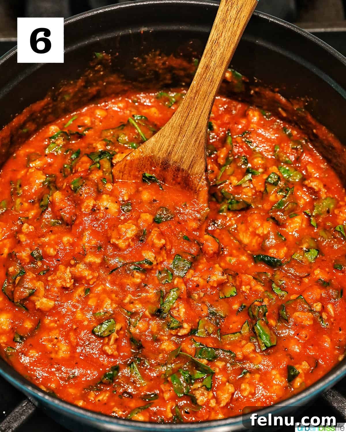 Creamy Vegan Lasagna 16 wooden spoon stirring ground turkey marinara sauce in a dutch oven.