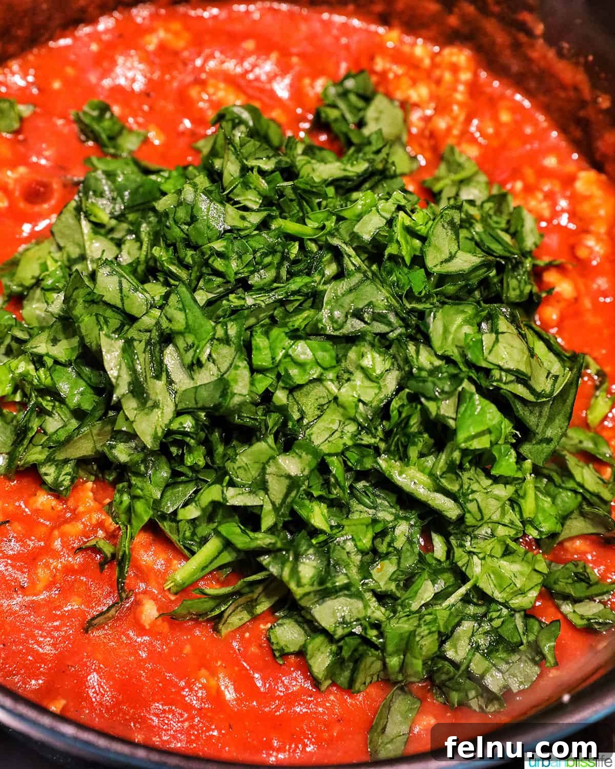 Creamy Vegan Lasagna 17 chopped spinach added to pasta sauce in a pan.