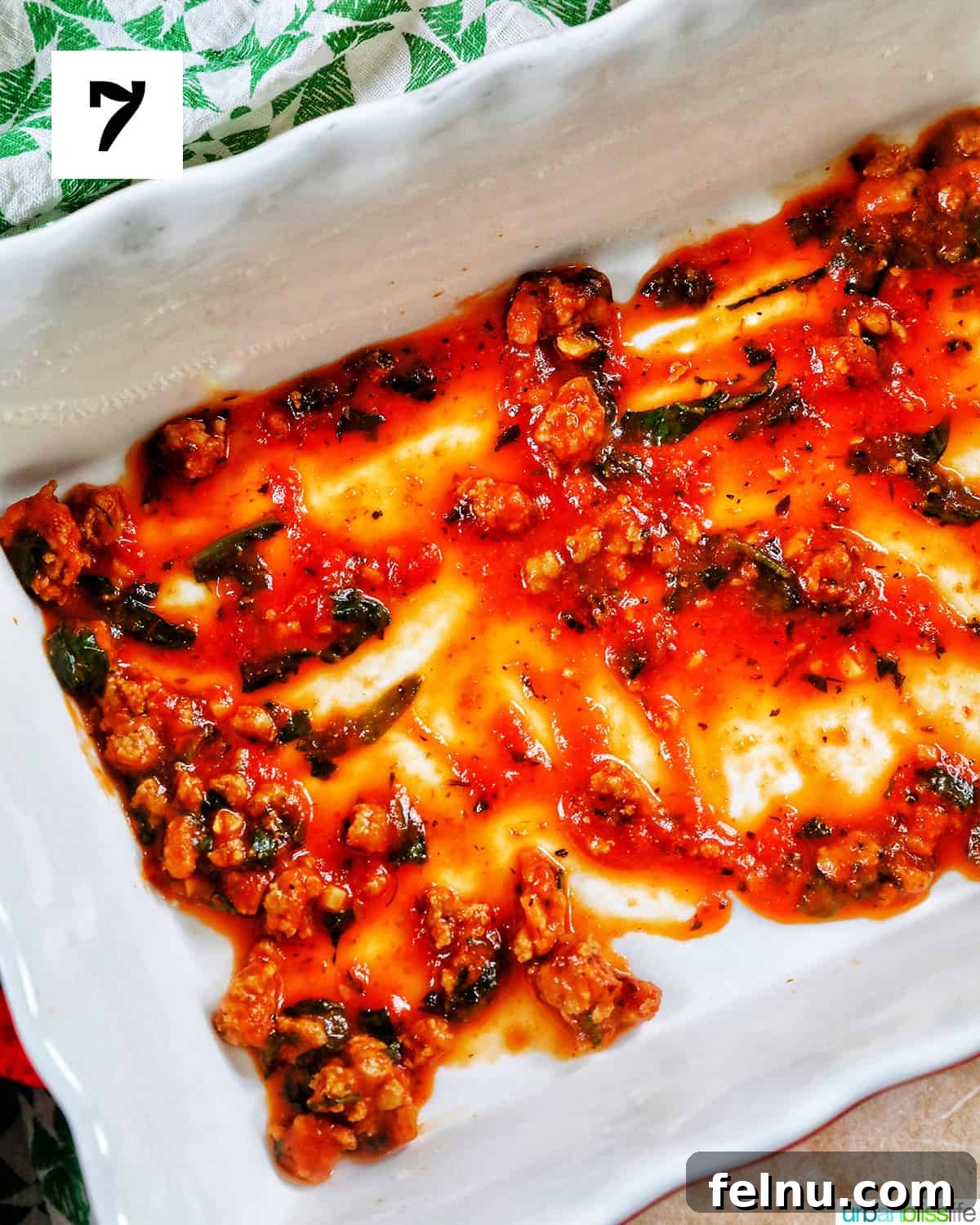 Creamy Vegan Lasagna 18 white baking dish with light pasta sauce smeared in a thin layer across the bottom.
