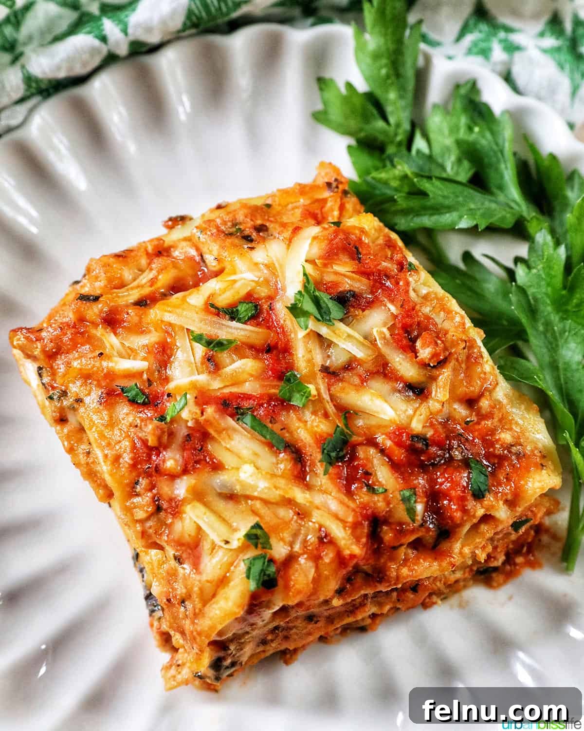 Creamy Vegan Lasagna 3 top view of multi-layered dairy free lasagna on a white plate with parsley on the side.