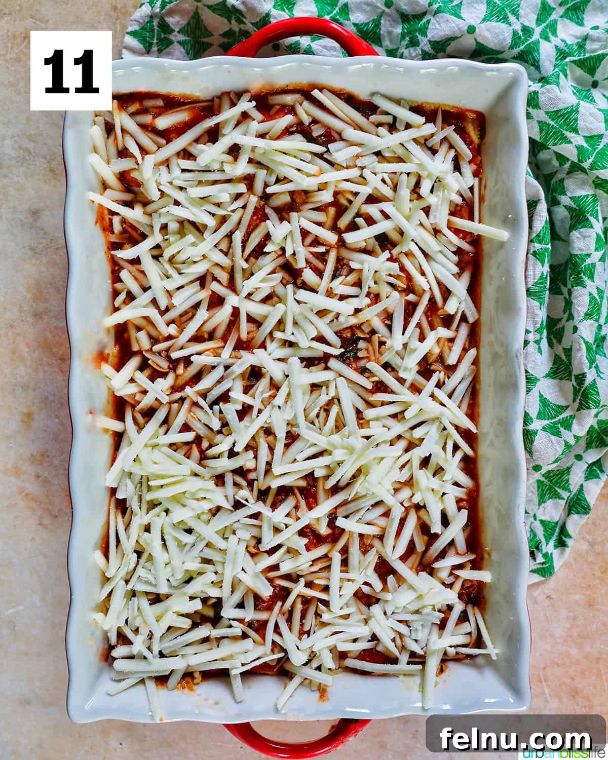 Creamy Vegan Lasagna 23 shredded dairy free mozzarella cheese added to the top layer of dairy free lasagna in a baking dish with red handles.