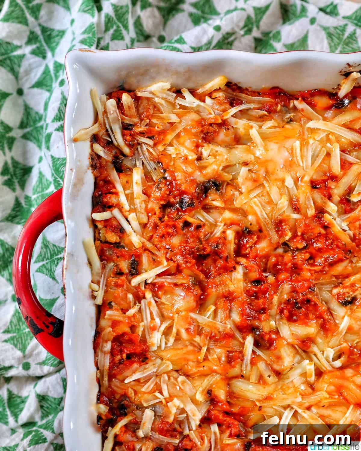 Creamy Vegan Lasagna 26 half side of a baking dish with red handle, filled with dairy free lasagna on a green and white napkin.