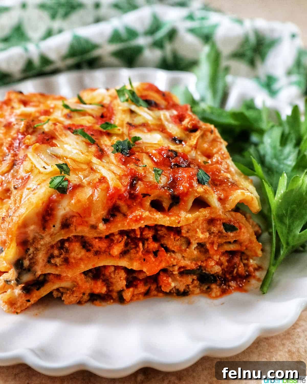 Creamy Vegan Lasagna 27 side view of multi-layered dairy free lasagna on a white plate with green and white napkin in background.