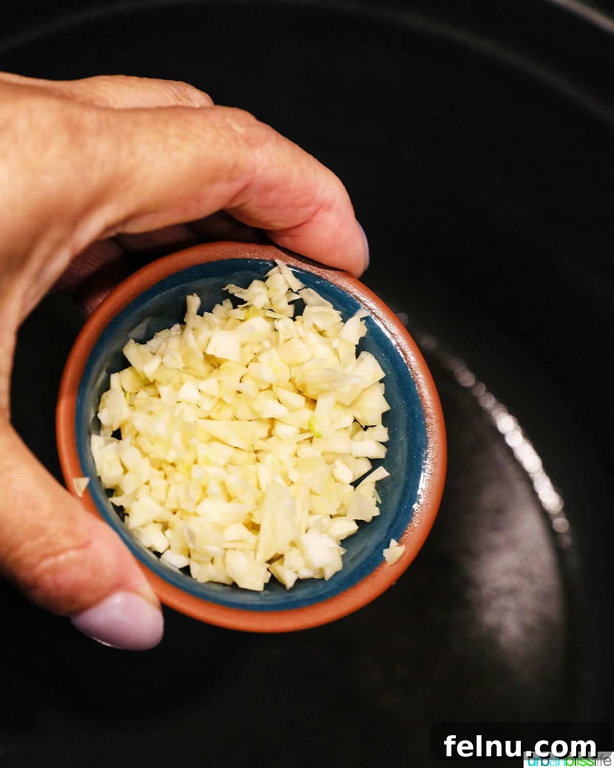 Creamy Vegan Lasagna 9 hand holding a pinch bowl full of minced garlic adding to a dutch oven pan or pot.