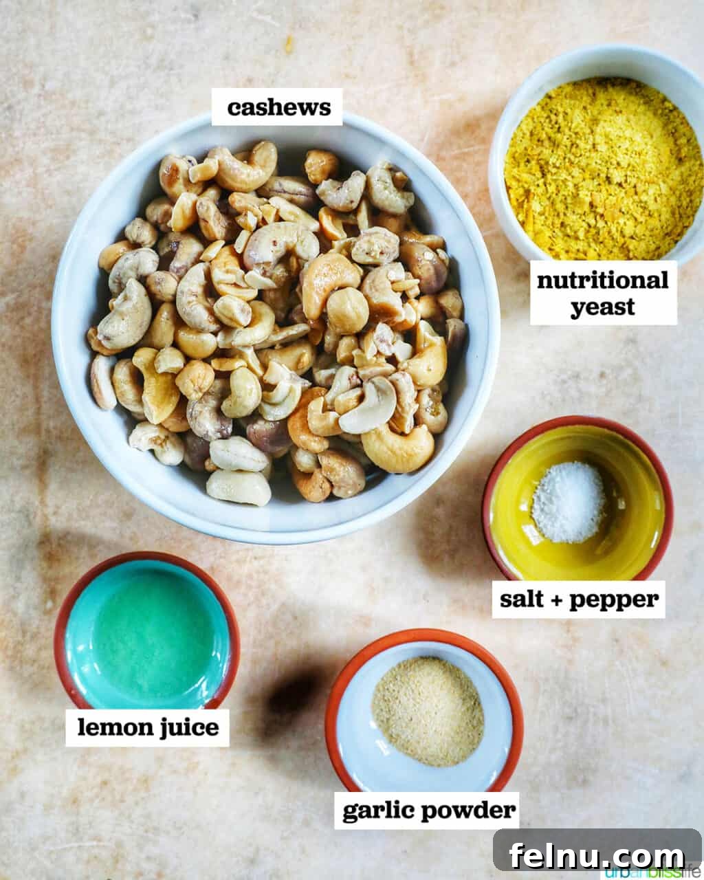 Creamy Vegan Cashew Cheese 4 Small bowls containing the key ingredients for Vegan Cashew Cheese – cashews, nutritional yeast, lemon juice, and garlic powder – neatly arranged on a vibrant yellow table.