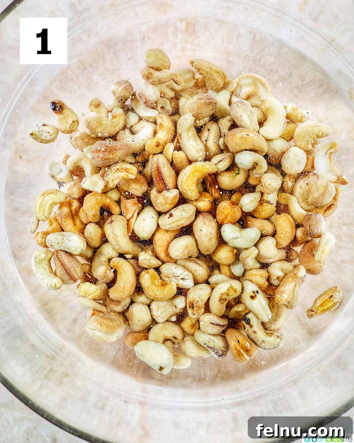 Creamy Vegan Cashew Cheese 5 Raw cashews soaking in a clear glass bowl of water on a yellow tabletop, demonstrating the first step of the recipe.
