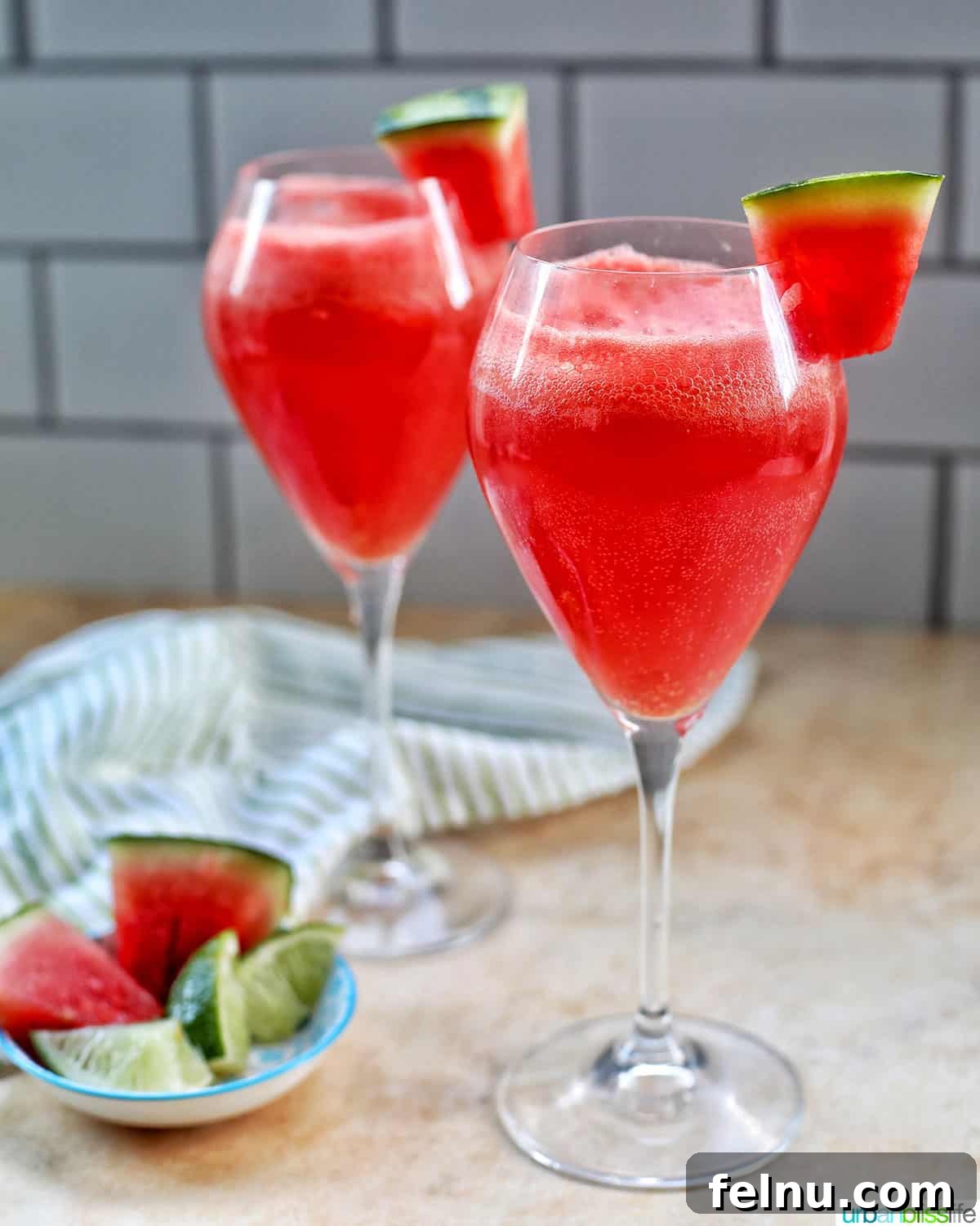 Watermelon Sunset Fizz 11 Two perfectly poured Watermelon Mimosas in flutes, with a bottle of sparkling wine and artistic watermelon slices in the background, ready to be enjoyed on a sunny day.