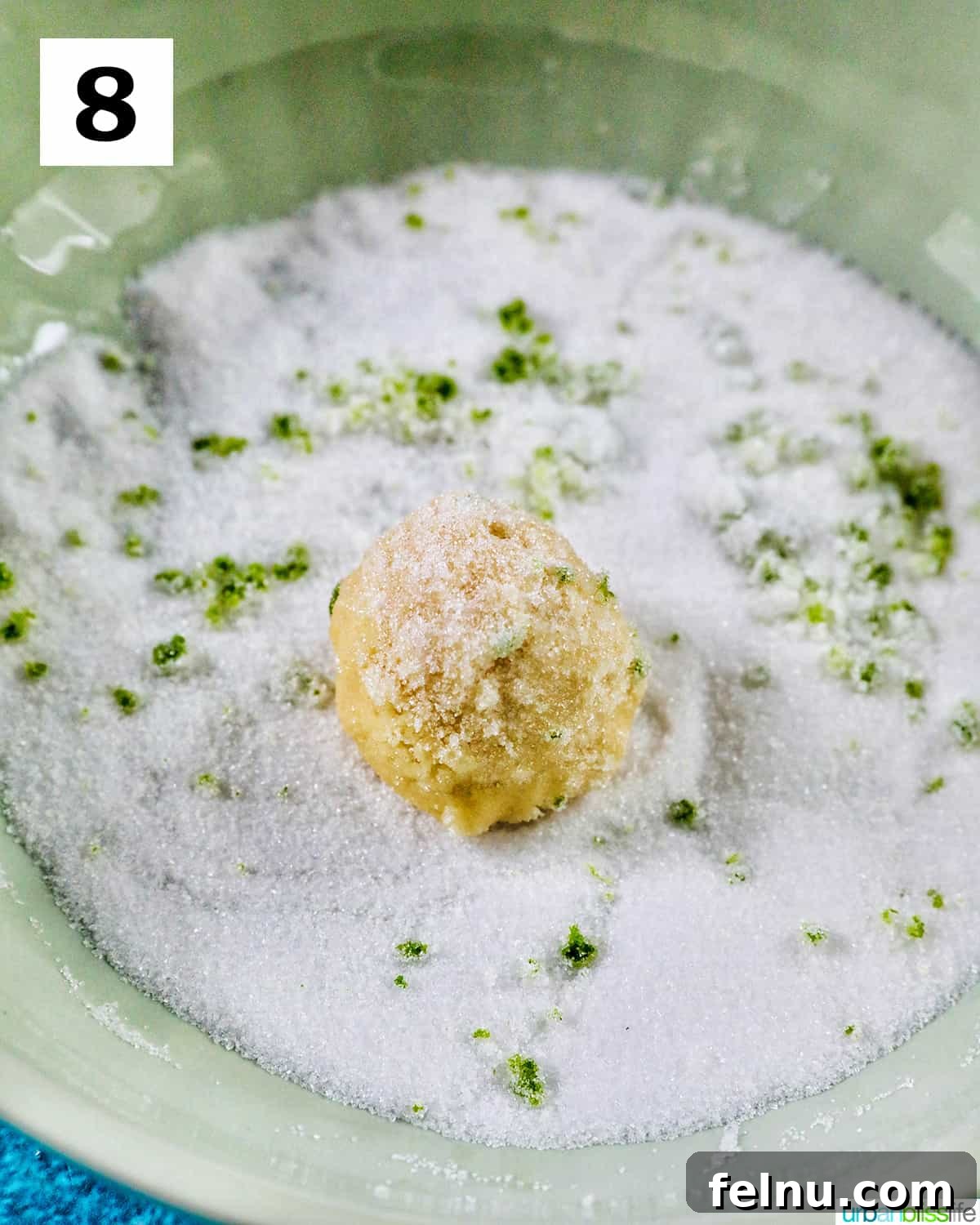 Tangy Key Lime Delights 17 A key lime cookie dough ball being rolled thoroughly in a mixture of granulated sugar and key lime zest, ensuring complete coating.