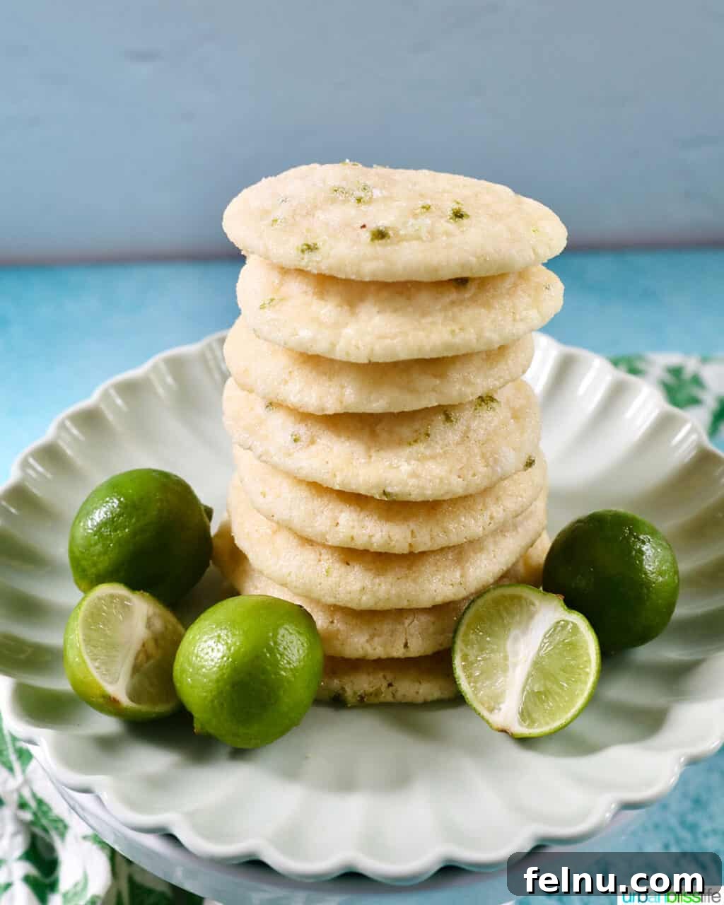 Tangy Key Lime Delights 20 A charming stack of golden-edged key lime cookies arranged on a scalloped white plate, surrounded by fresh green key limes, ready to be enjoyed.