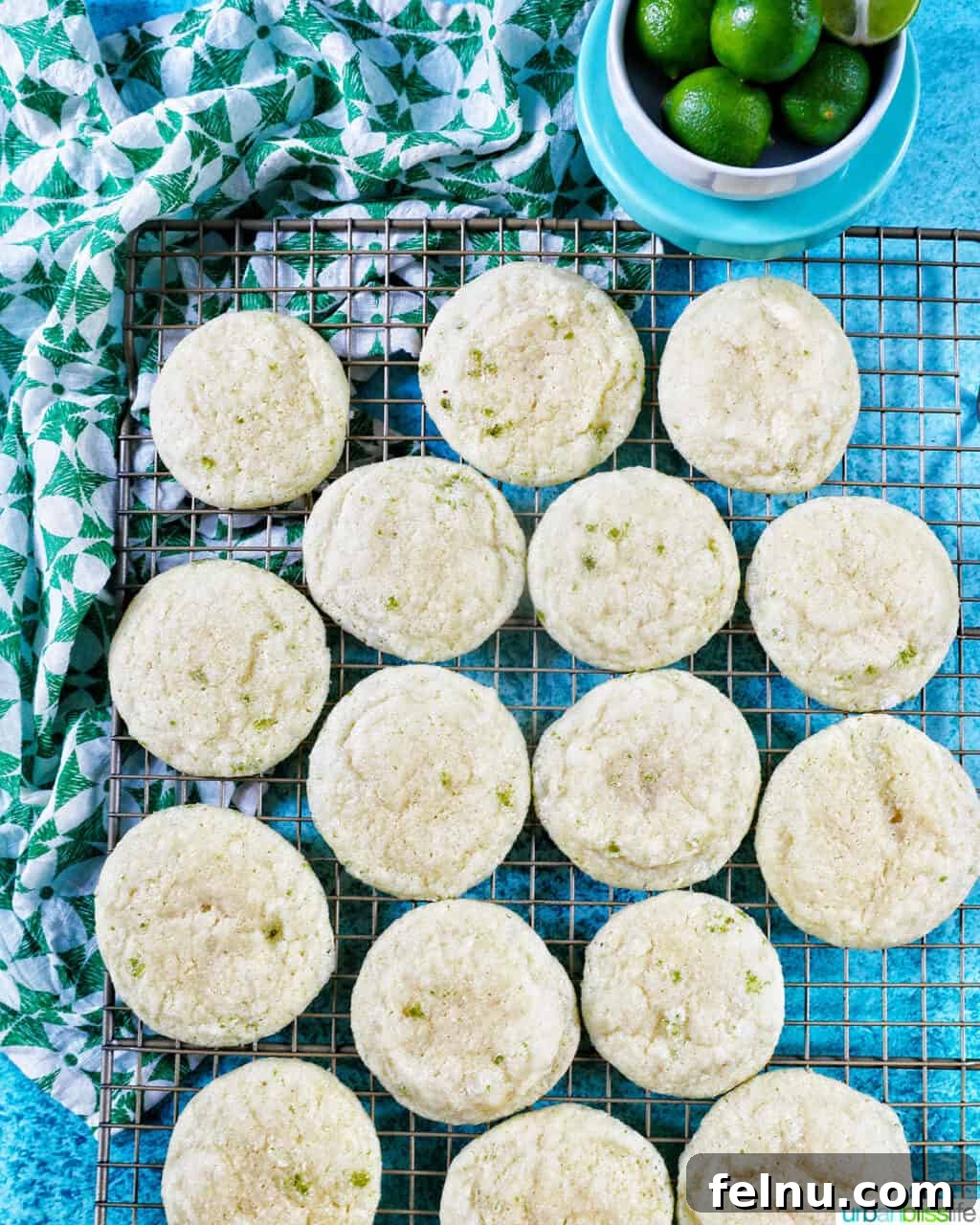 Tangy Key Lime Delights 3 Several freshly baked key lime cookies cooling on a wire rack, with a small bowl of key limes for garnish in the background.