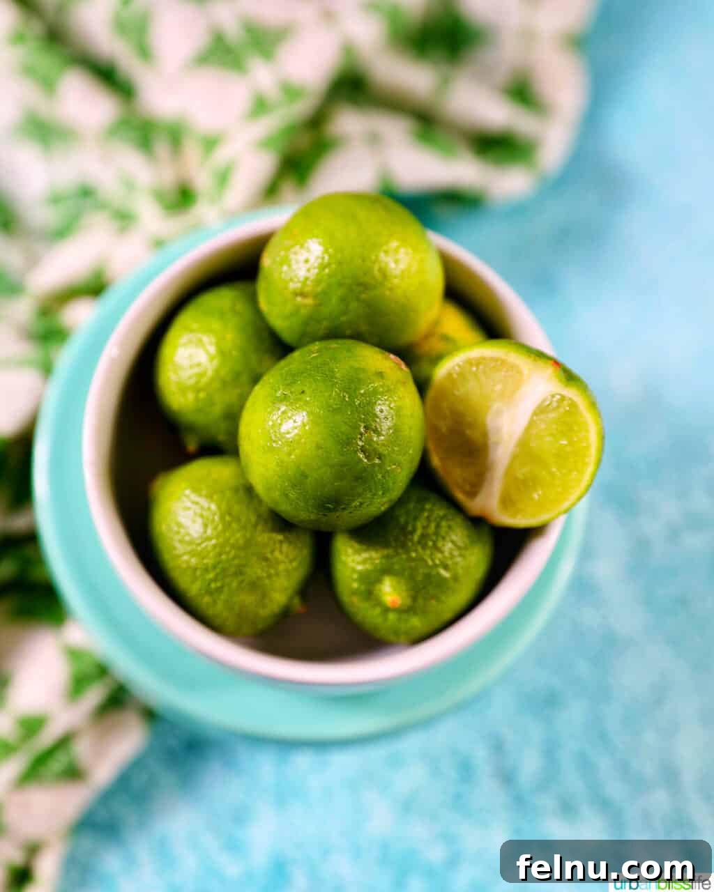 Tangy Key Lime Delights 4 A small bowl overflowing with vibrant green key limes, set against a bright blue background with a green and white striped napkin.