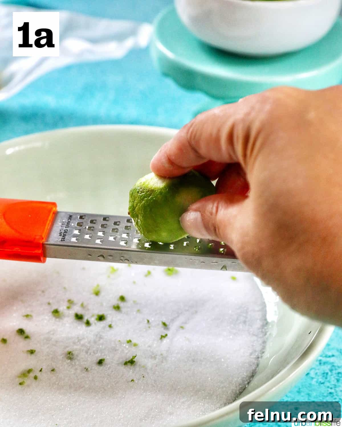 Tangy Key Lime Delights 6 A hand zesting a vibrant key lime directly over a bowl filled with granulated sugar, capturing the aromatic oils.