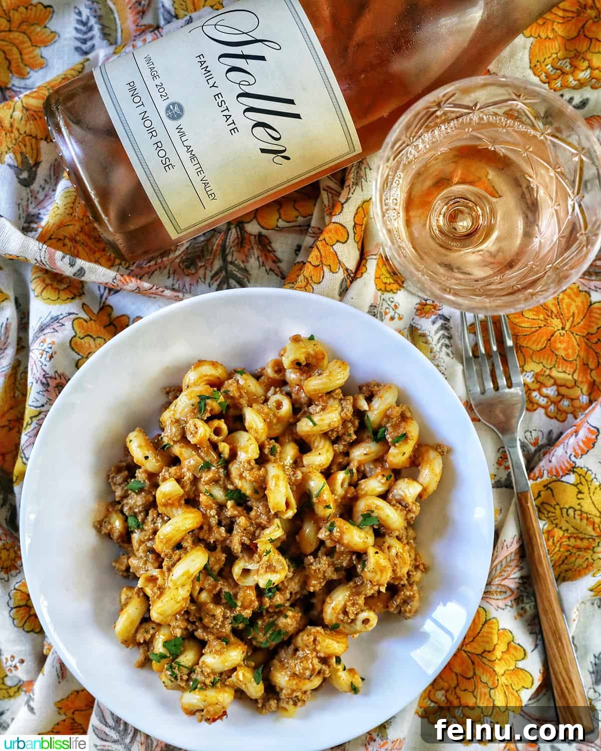 Creamy Dairy-Free Cheeseburger Mac Skillet 14 A bowl of dairy-free cheeseburger pasta served on colorful napkins, accompanied by a bottle and a glass of refreshing rosé wine.